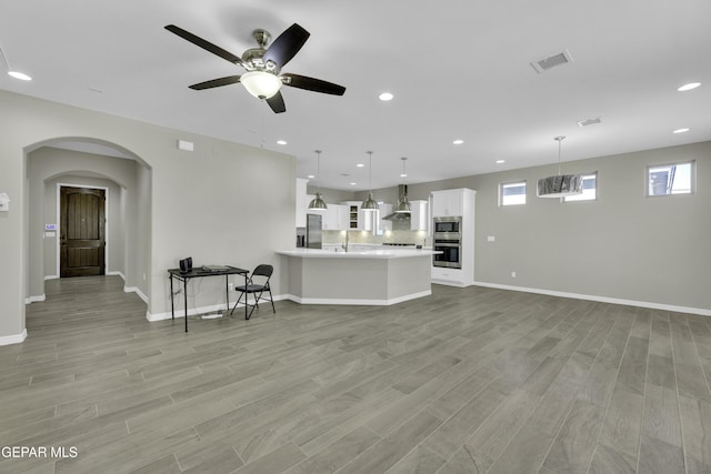 unfurnished living room with sink, ceiling fan with notable chandelier, and light wood-type flooring