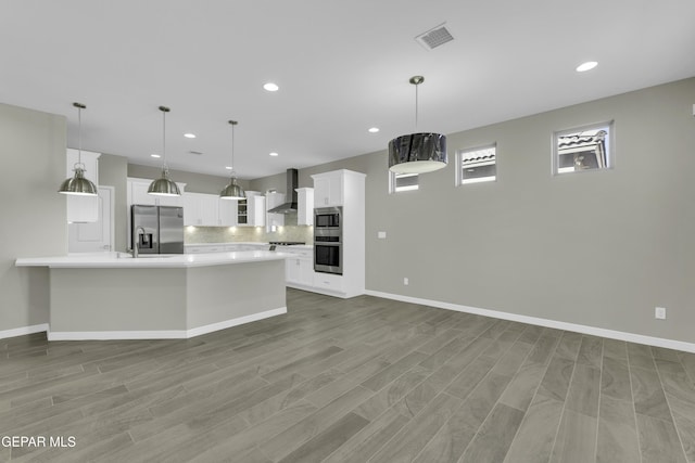 kitchen featuring appliances with stainless steel finishes, backsplash, wall chimney range hood, pendant lighting, and white cabinets