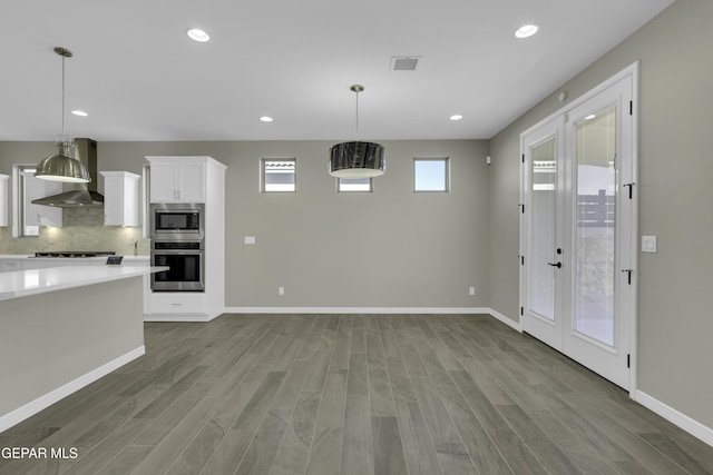 interior space featuring appliances with stainless steel finishes, backsplash, wall chimney exhaust hood, decorative light fixtures, and white cabinetry