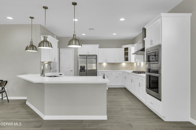 kitchen with pendant lighting, wall chimney range hood, sink, appliances with stainless steel finishes, and white cabinetry