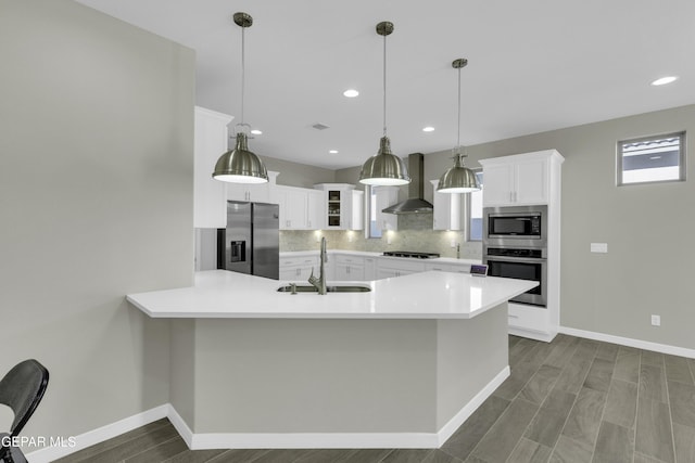 kitchen featuring white cabinets, stainless steel appliances, hanging light fixtures, and wall chimney range hood