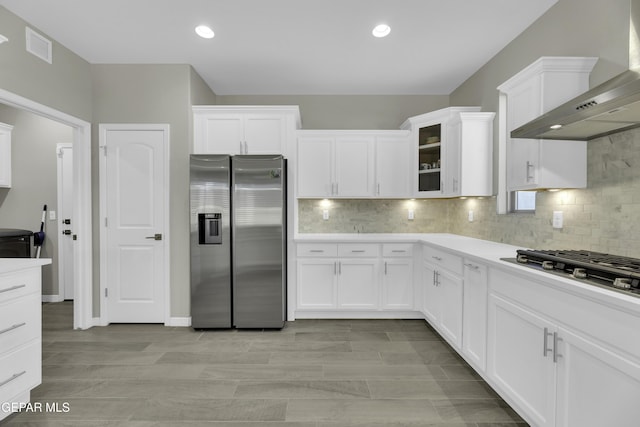 kitchen featuring white cabinets, backsplash, stainless steel appliances, and wall chimney exhaust hood