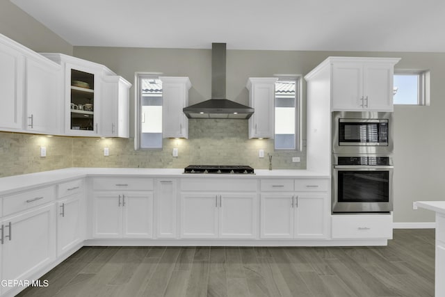 kitchen featuring wall chimney exhaust hood, decorative backsplash, light hardwood / wood-style floors, white cabinetry, and stainless steel appliances