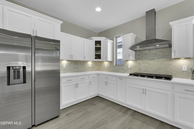 kitchen with wall chimney range hood, gas cooktop, stainless steel fridge with ice dispenser, decorative backsplash, and white cabinets