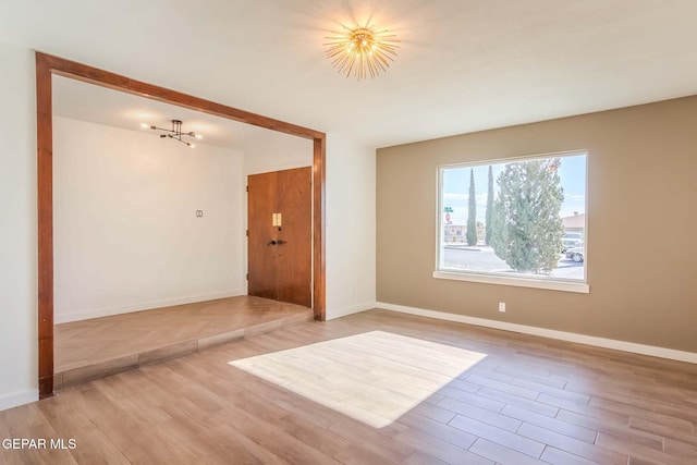 unfurnished room with a chandelier and light wood-type flooring