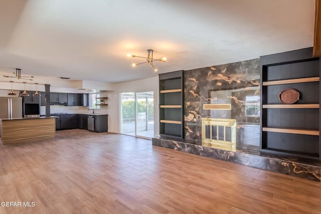 unfurnished living room with sink, built in shelves, a fireplace, wood-type flooring, and a chandelier