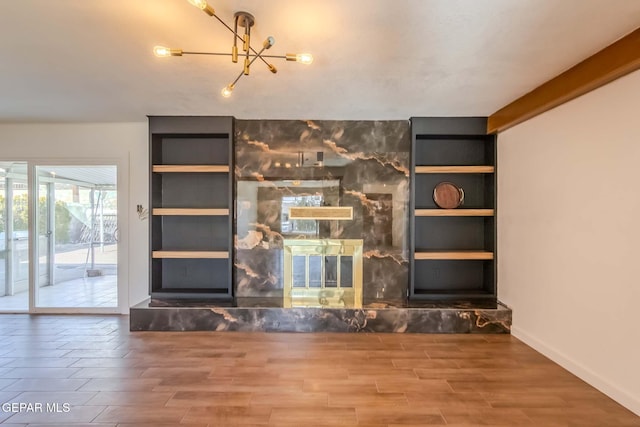 unfurnished living room with a stone fireplace, built in features, and an inviting chandelier