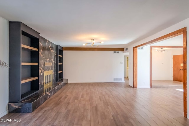 unfurnished living room featuring a tile fireplace, built in features, and hardwood / wood-style floors