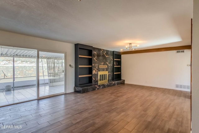 unfurnished living room featuring a chandelier, built in shelves, a stone fireplace, and wood-type flooring