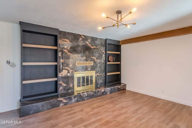 unfurnished living room with a fireplace, built in features, an inviting chandelier, and hardwood / wood-style flooring