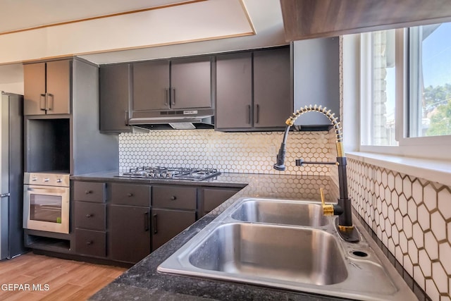 kitchen featuring appliances with stainless steel finishes, tasteful backsplash, dark stone counters, sink, and light hardwood / wood-style floors