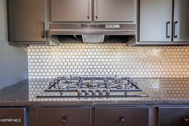 kitchen with stainless steel gas stovetop, decorative backsplash, dark stone countertops, and range hood