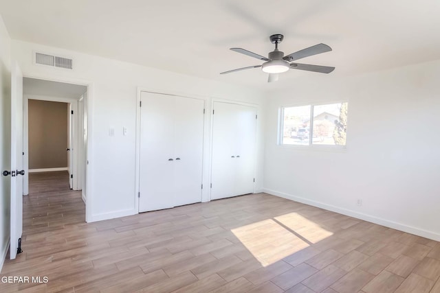 unfurnished bedroom with ceiling fan and multiple closets