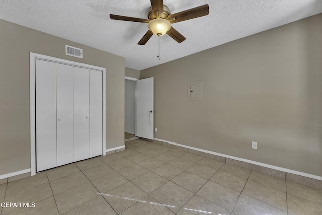 unfurnished bedroom featuring ceiling fan, light tile patterned floors, a textured ceiling, and a closet