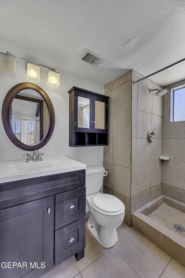 bathroom with vanity, tile patterned floors, toilet, a textured ceiling, and a tile shower