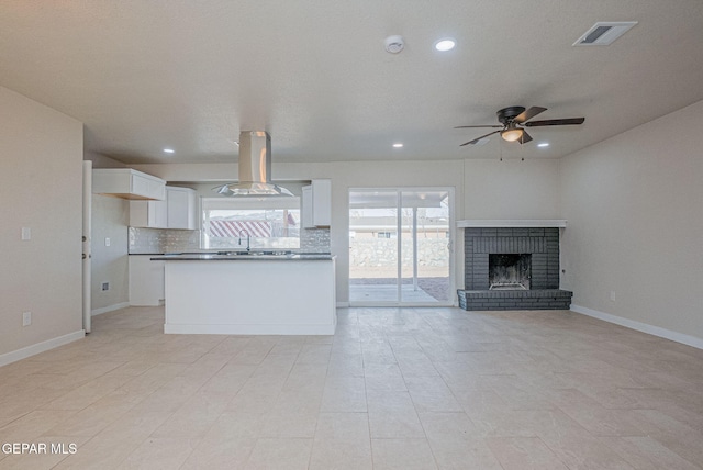 kitchen featuring a brick fireplace, island range hood, ceiling fan, sink, and white cabinets