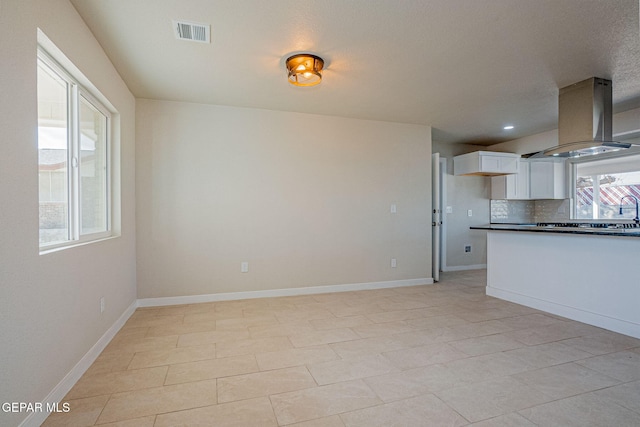 kitchen with island range hood, white cabinetry, backsplash, and light tile patterned floors