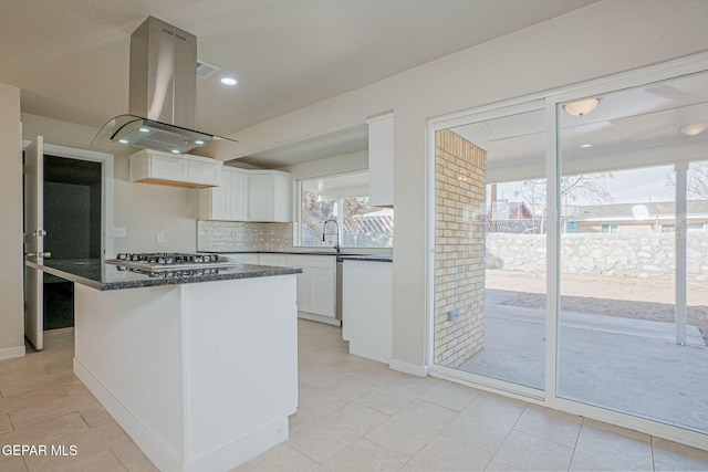 kitchen with stainless steel gas cooktop, tasteful backsplash, island exhaust hood, dark stone counters, and white cabinets