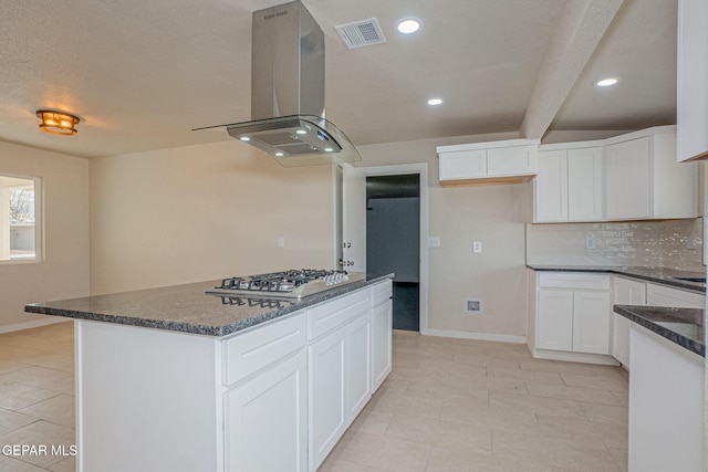 kitchen with dark stone countertops, a kitchen island, white cabinetry, island exhaust hood, and stainless steel gas cooktop