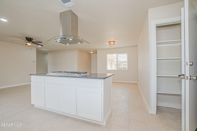 kitchen featuring white gas stovetop, ceiling fan, dark stone countertops, island range hood, and white cabinetry