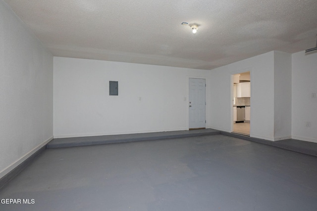 spare room featuring a textured ceiling, concrete floors, and electric panel