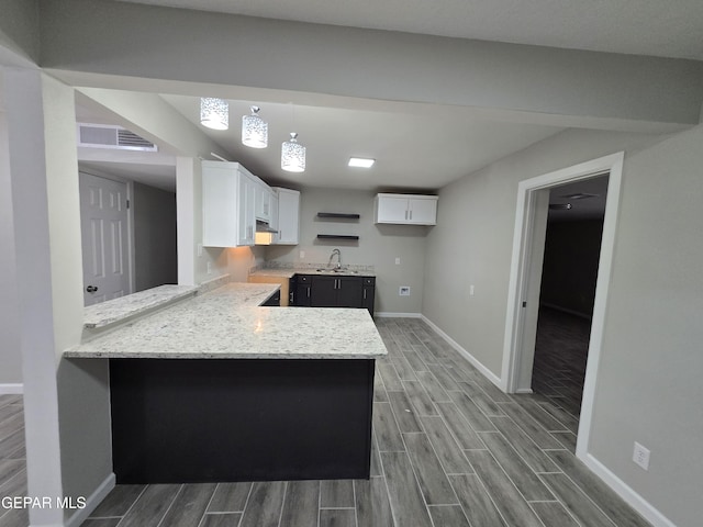 kitchen featuring sink, kitchen peninsula, light stone countertops, decorative light fixtures, and white cabinetry