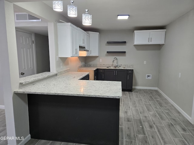 kitchen with white cabinetry, sink, light stone counters, kitchen peninsula, and pendant lighting