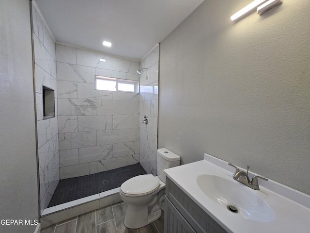 bathroom with a tile shower, vanity, and toilet