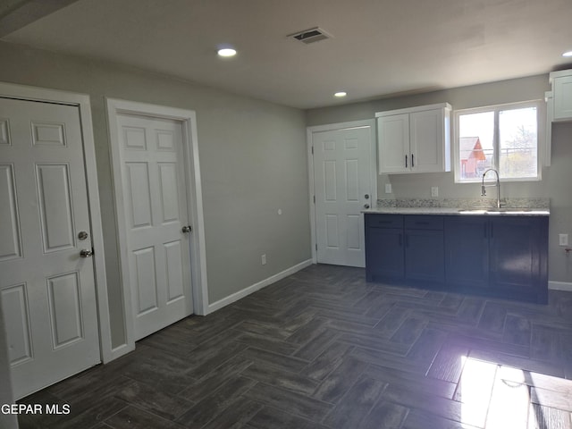 kitchen with white cabinets, light stone counters, dark parquet flooring, and sink