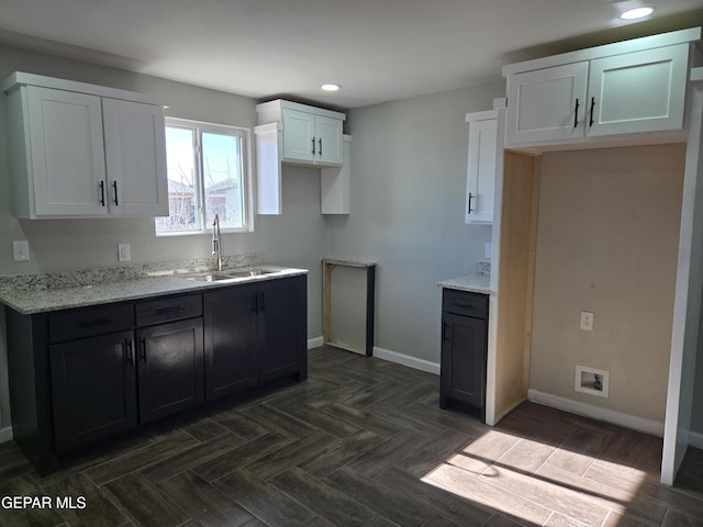 kitchen featuring light stone counters, white cabinetry, and sink