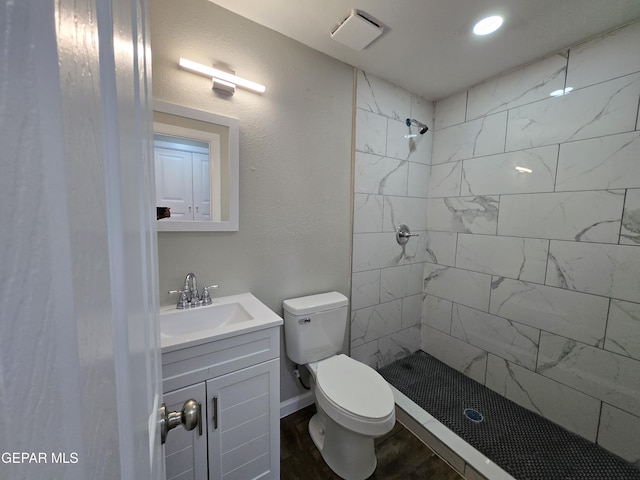 bathroom featuring hardwood / wood-style flooring, vanity, toilet, and tiled shower