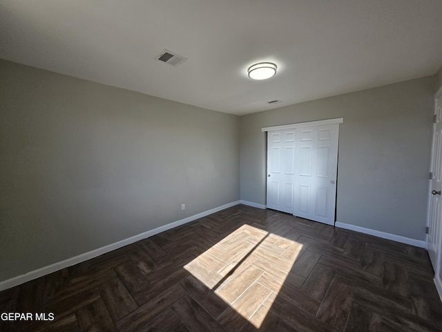 unfurnished bedroom with dark parquet flooring and a closet