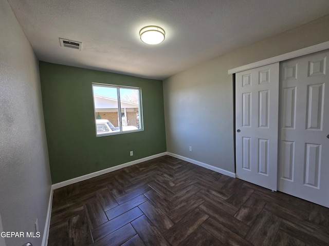 unfurnished bedroom featuring dark parquet flooring, a textured ceiling, and a closet