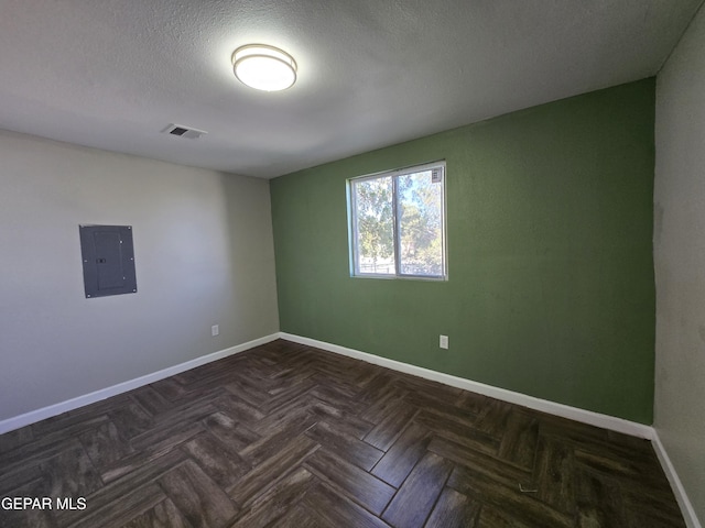 empty room featuring dark parquet floors, a textured ceiling, and electric panel