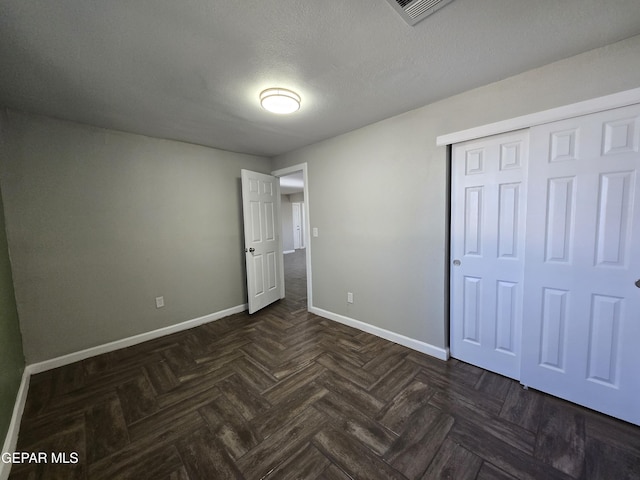 unfurnished bedroom featuring dark parquet flooring, a closet, and a textured ceiling