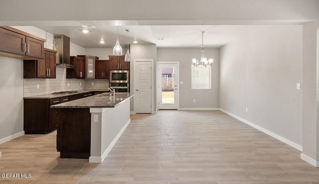 kitchen with stainless steel appliances, hanging light fixtures, wall chimney exhaust hood, and a kitchen island with sink