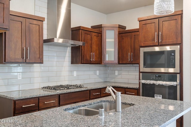 kitchen with sink, wall chimney exhaust hood, light stone countertops, appliances with stainless steel finishes, and tasteful backsplash