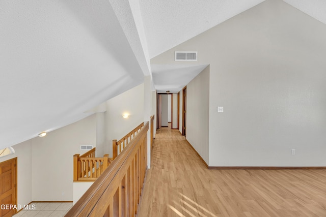 corridor featuring a textured ceiling, light hardwood / wood-style floors, and vaulted ceiling