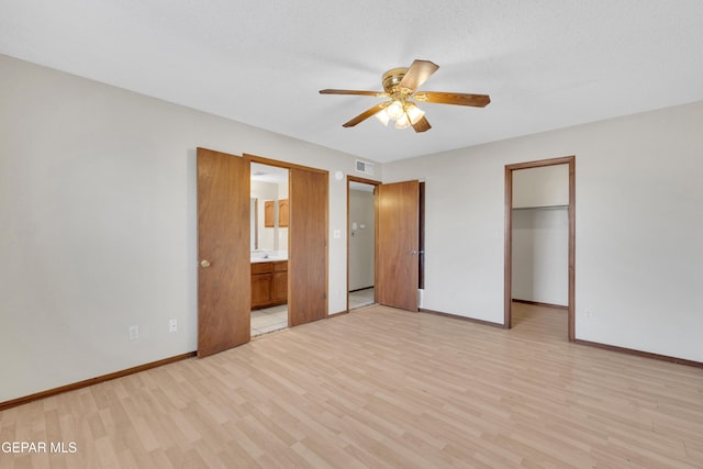 unfurnished bedroom featuring light wood-type flooring, ensuite bathroom, a spacious closet, and ceiling fan