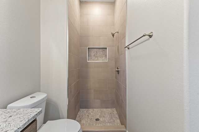 bathroom with tiled shower, vanity, and toilet