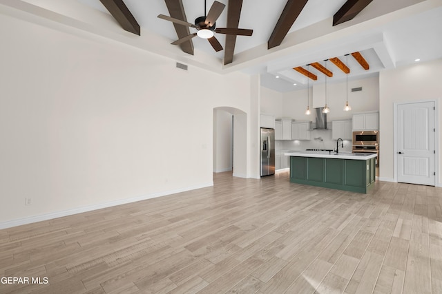 unfurnished living room with beam ceiling, ceiling fan, light hardwood / wood-style floors, and a high ceiling