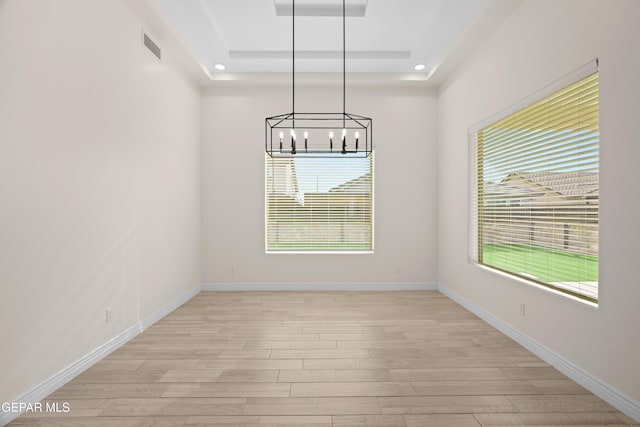 unfurnished dining area featuring a raised ceiling, light wood-type flooring, and a wealth of natural light