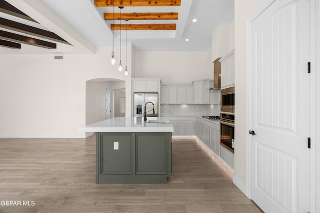 kitchen featuring pendant lighting, sink, an island with sink, appliances with stainless steel finishes, and beamed ceiling