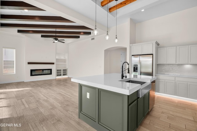 kitchen with white cabinets, ceiling fan, an island with sink, appliances with stainless steel finishes, and beamed ceiling