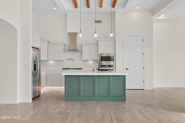 kitchen with appliances with stainless steel finishes, a towering ceiling, wall chimney exhaust hood, white cabinets, and hanging light fixtures