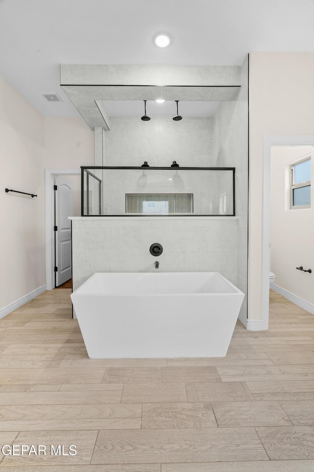 bathroom with a tub to relax in and toilet