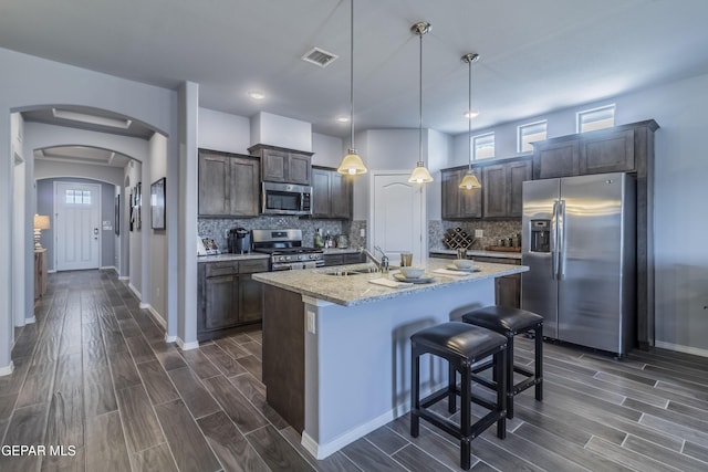 kitchen with backsplash, sink, hanging light fixtures, an island with sink, and appliances with stainless steel finishes