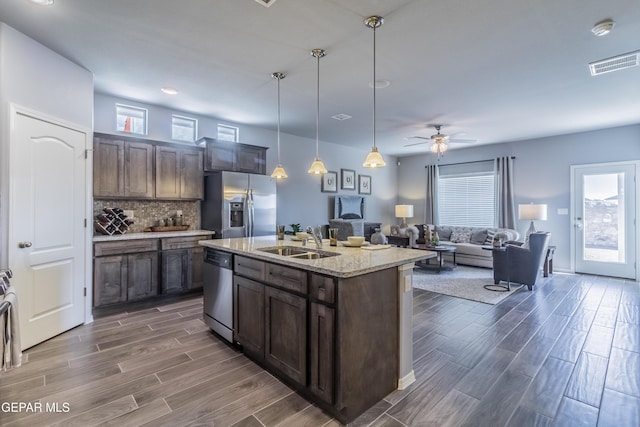 kitchen with appliances with stainless steel finishes, ceiling fan, sink, decorative light fixtures, and an island with sink