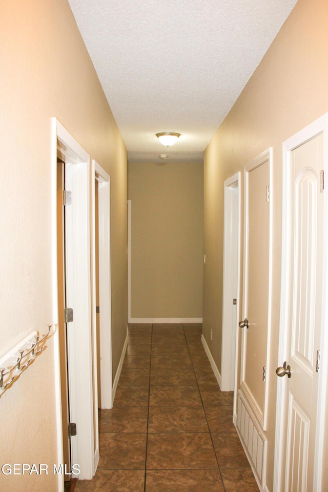 corridor featuring a textured ceiling and dark tile patterned floors