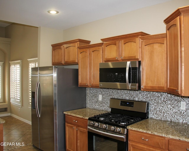 kitchen featuring tile patterned flooring, light stone countertops, backsplash, and appliances with stainless steel finishes